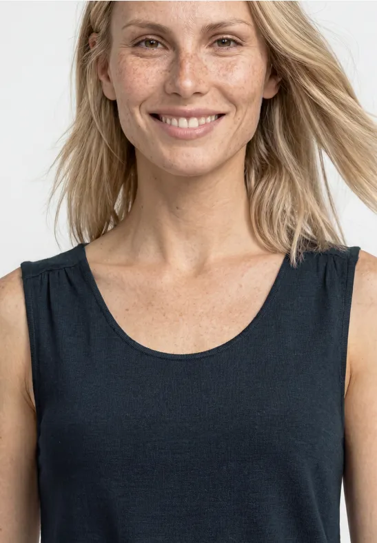 Femme blonde aux cheveux lâchés porte un débardeur noir, épaules et cou dégagés.