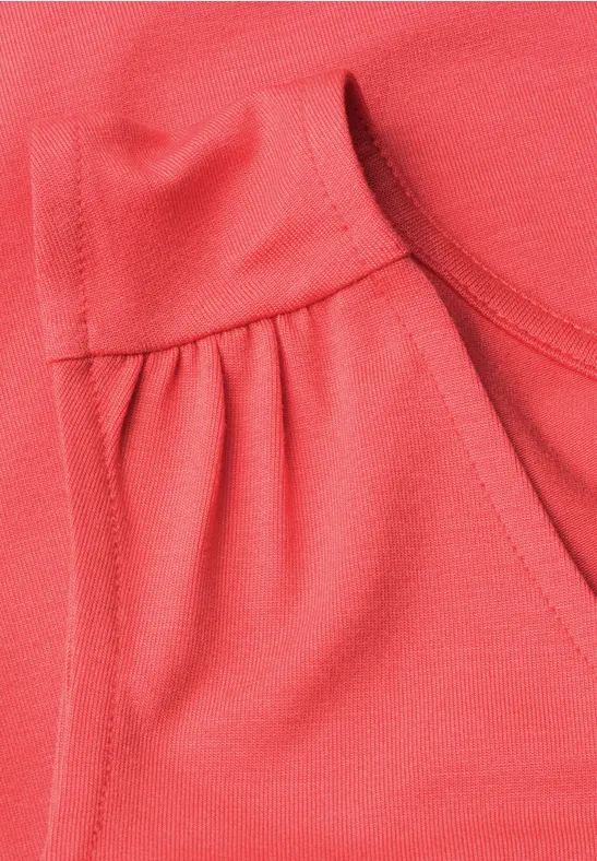 Close-up van een koraalkleurig shirt met ronde hals en plooien aan de zijkant.
