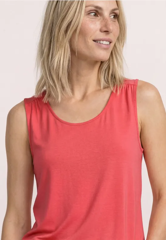 Vrouw met blond haar draagt een rood mouwloos shirt.