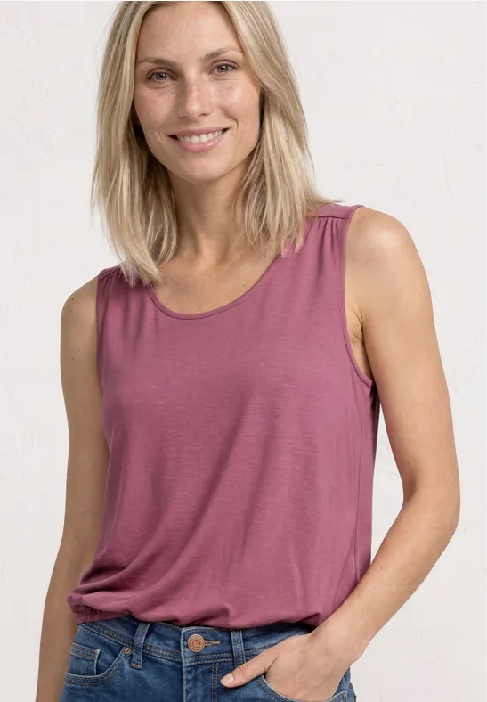 Vrouw met blond haar draagt een losvallend pruimkleurig topje en een spijkerbroek.