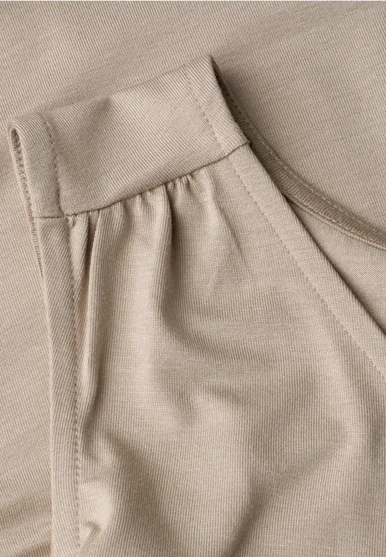 Close-up van een beige jersey kledingstuk met ronde hals en geplooide schouder