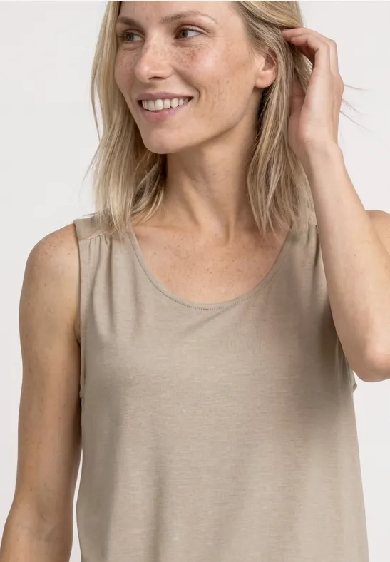 Een lachende vrouw draagt een mouwloze beige top voor een neutrale achtergrond.