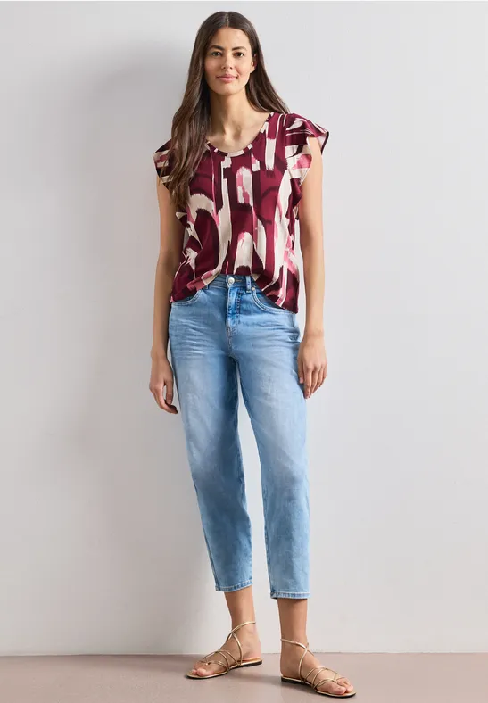Een vrouw draagt een T-shirt met korte mouwen en print, blauwe jeans en sandalen.