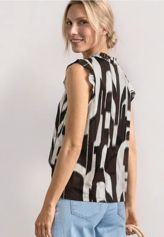 Vrouw van achteren in een mouwloze top met zwart-wit abstract motief en een jeans.