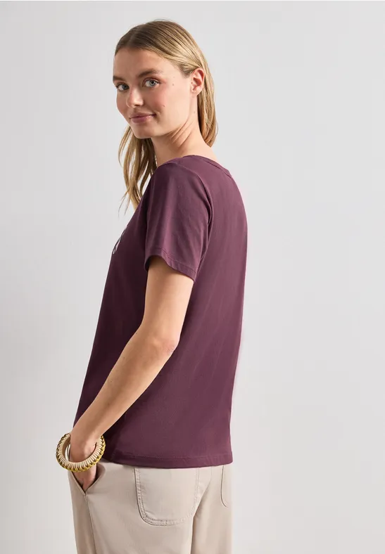 Zijaanzicht van persoon in paars T-shirt en beige broek, gezicht wazig gemaakt.