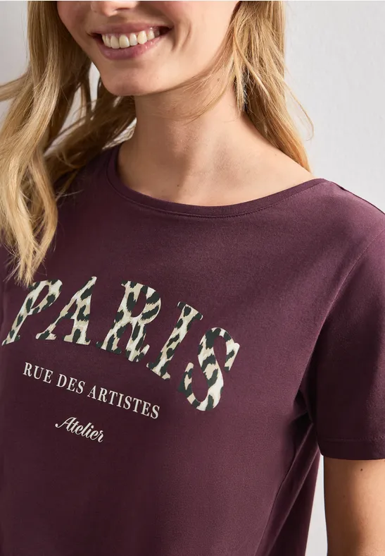 Close-up van een bordeauxroze T-shirt met bloemenprint 'PARIS' en de tekst 'Rue des Artistes'.