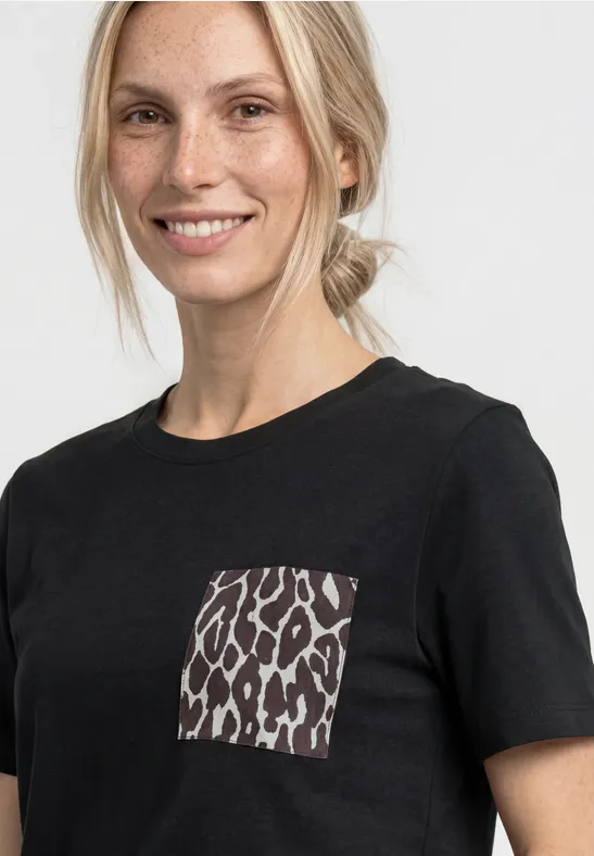 Een vrouw draagt een zwart t-shirt met een leopardprint zakje tegen een lichte achtergrond.