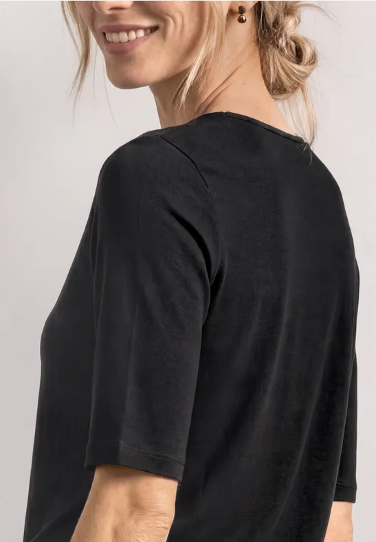 Frau im schwarzen Halbarmshirt, von hinten fotografiert, mit lockerem Dutt und dezentem Ohrschmuck.