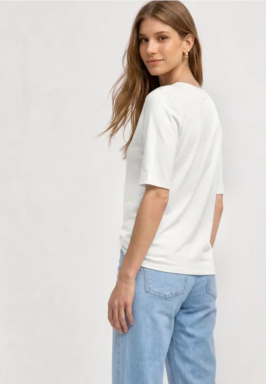 Frau von hinten in weißem T-Shirt und blauen Jeans vor hellem Hintergrund.