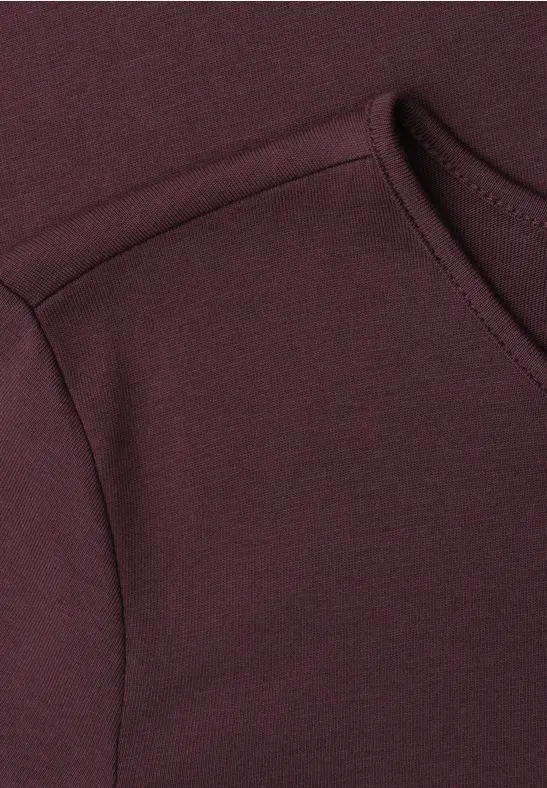 Close-up van een bordeauxrood kledingstuk met zichtbare schouder- en halsnaad.