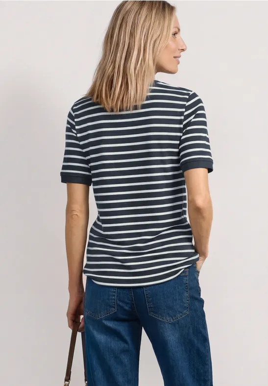 Vrouw van achteren in een gestreept T-shirt en spijkerbroek, met een tas in haar rechterhand.
