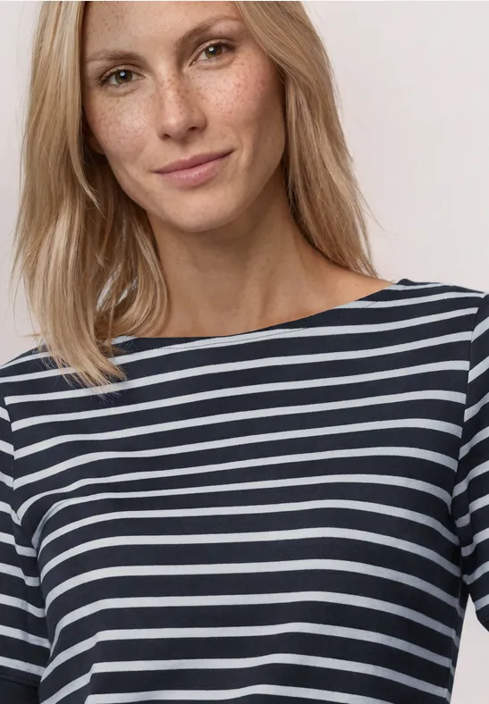 Vrouw in zwart-wit gestreepte top met boothals en driekwartmouwen tegen een neutrale achtergrond.