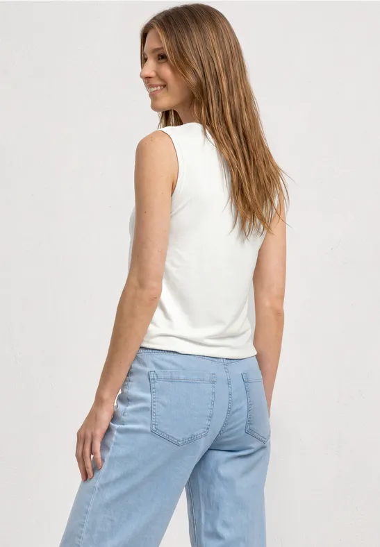 Seitliche Rückansicht einer Frau in weißem ärmellosem Top und hellblauen Jeans.