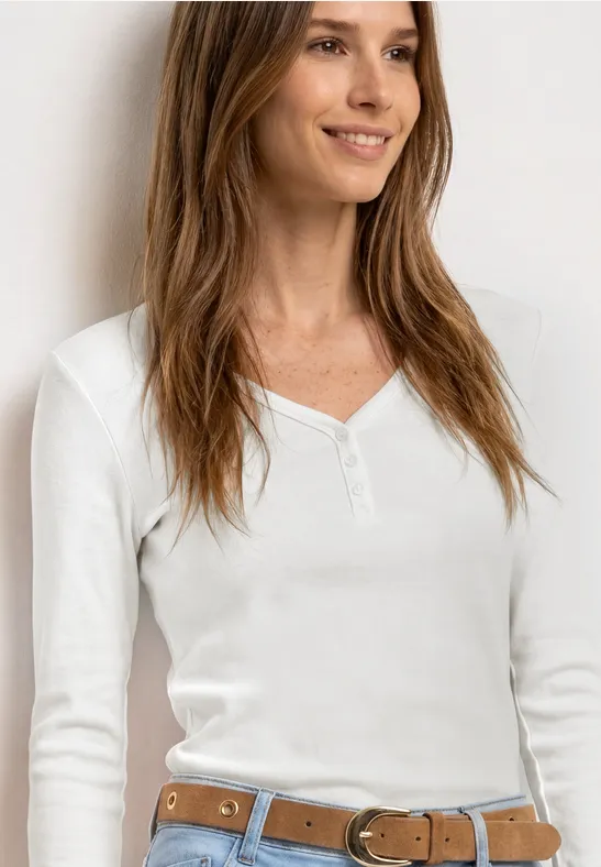 Femme souriante en haut blanc à manches longues, col en V, ceinture marron clair.
