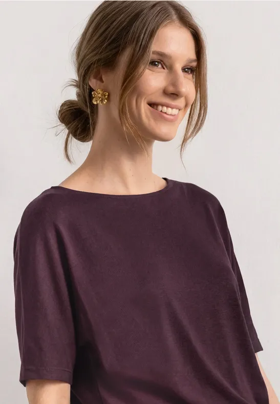 Vrouw met opgestoken haar draagt een eenvoudig paars T-shirt en gouden oorbel.