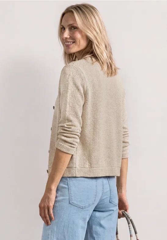 Femme vue de dos avec un gilet beige et un jean bleu, tenant un sac à main.