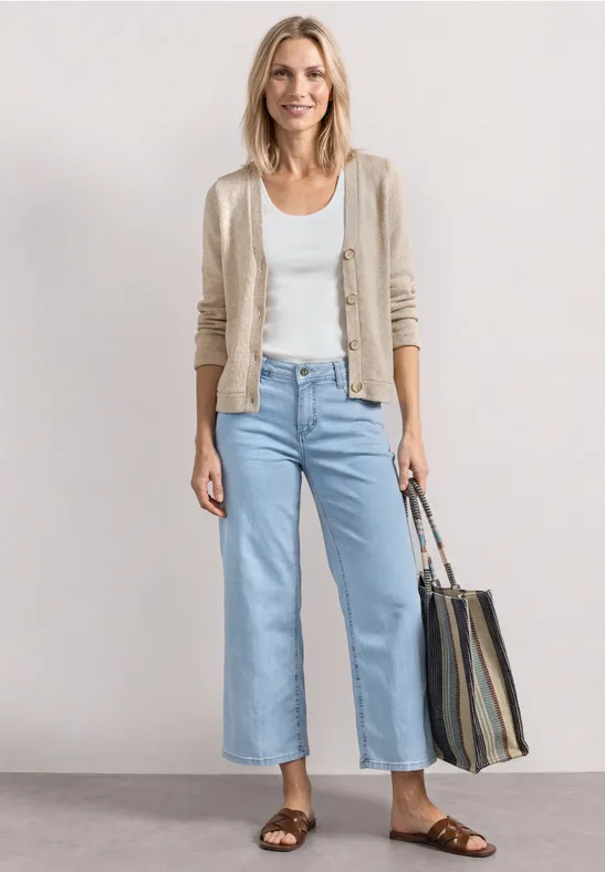 Femme en jean large bleu clair, débardeur blanc, gilet beige, sandales marron et sac rayé.