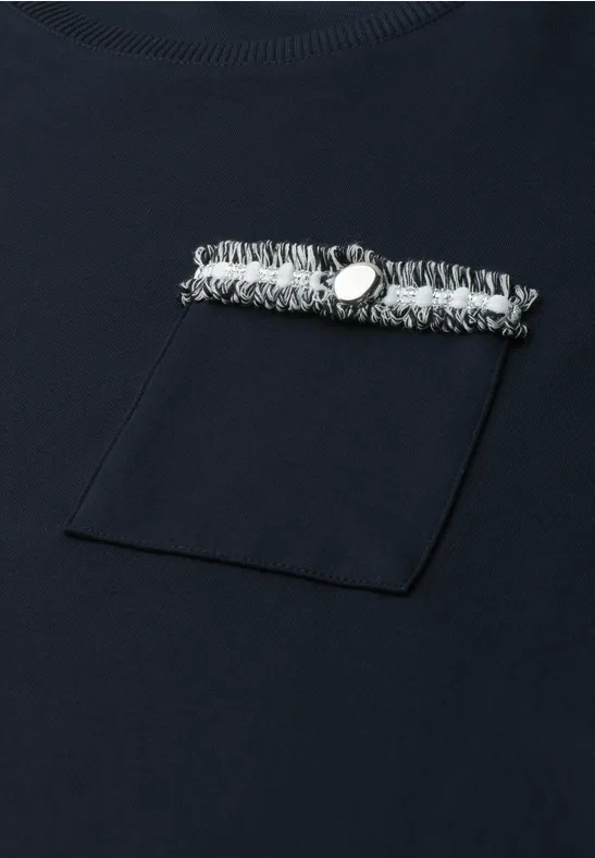 T-shirt bleu marine avec poche poitrine et bande effilochée ornée d’un bouton métallique.