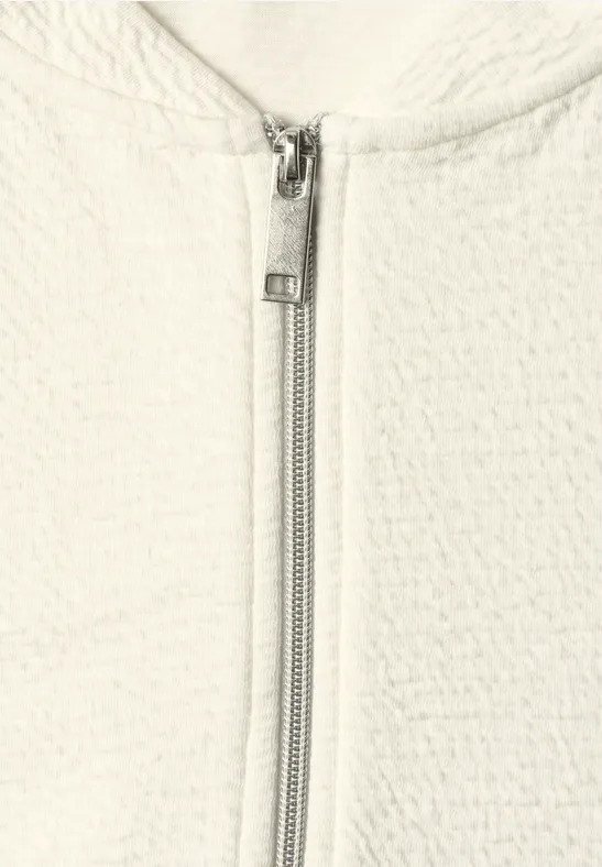 Gros plan d'une veste blanche texturée avec une fermeture éclair métallique centrale.