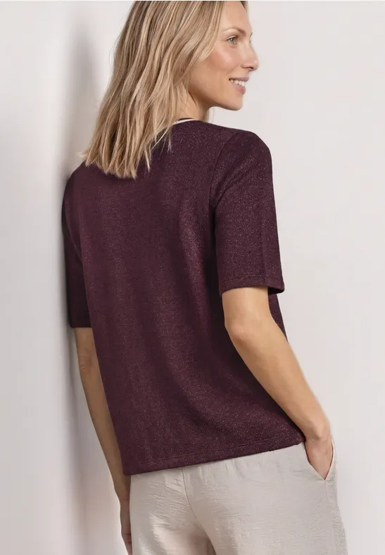Vrouw van achteren in een donkerpaars kort shirt en beige broek.