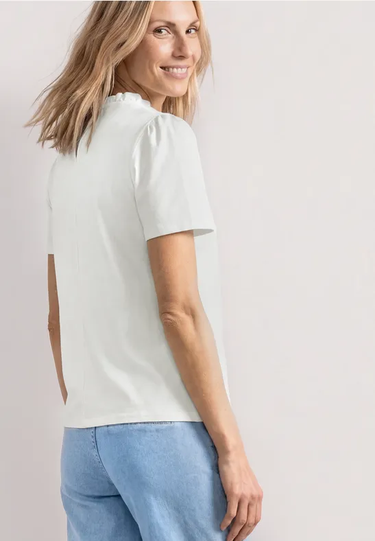 Eine Frau von hinten mit weißem T-Shirt und blauen Jeans vor neutralem Hintergrund.
