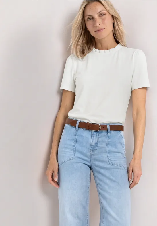 Eine Frau trägt ein weißes T-Shirt und hellblaue Jeans mit braunem Gürtel.