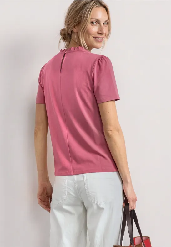 Vrouw van achteren met roze shirt, witte jeans en een handtas in de hand.