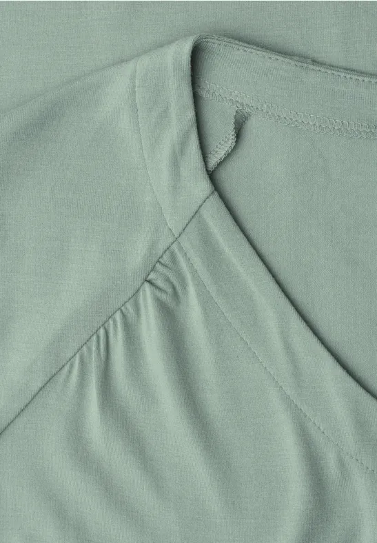 Gros plan d’un t-shirt vert pastel avec encolure en V et surpiqûres apparentes.