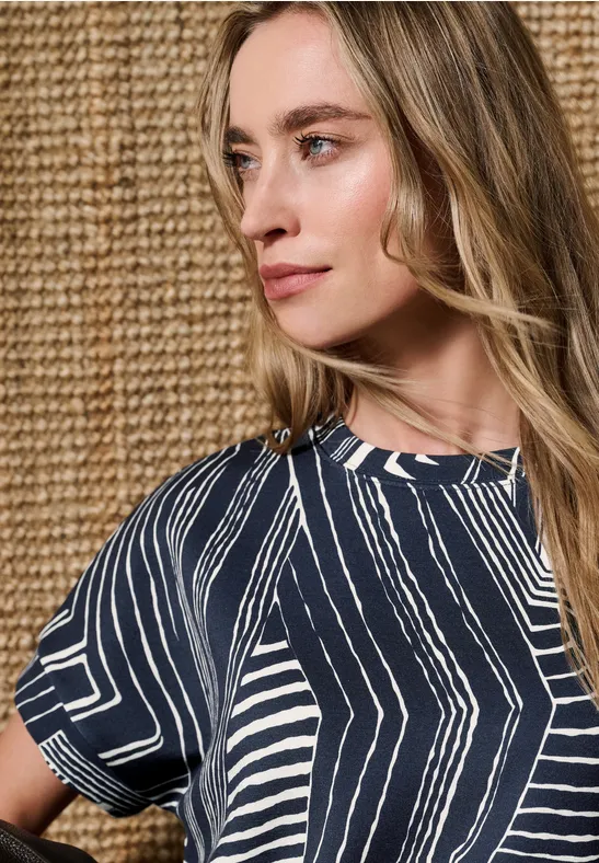 Femme portant un haut bleu et blanc devant un mur en osier beige.