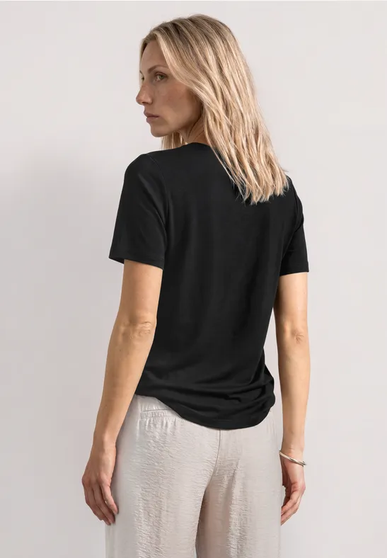 Eine Person steht mit dem Rücken zur Kamera, trägt ein schwarzes T-Shirt und helle Hose.