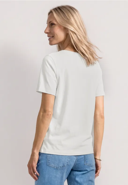 Frau von hinten in weißem T-Shirt und blauen Jeans vor neutralem Hintergrund.