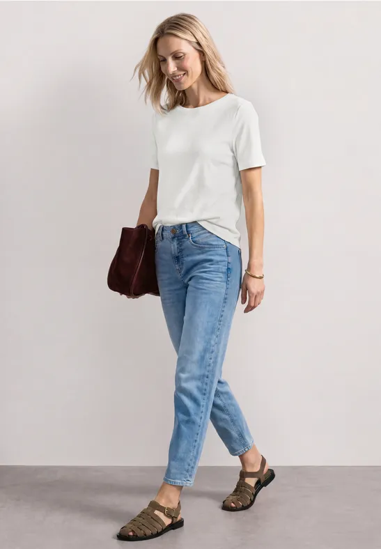 Frau in weißem T-Shirt, blauen Jeans, braunen Sandalen und Tasche.