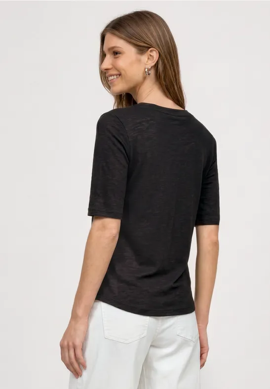 Rückenansicht einer Frau in schwarzem T-Shirt und weißen Jeans vor weißem Hintergrund.