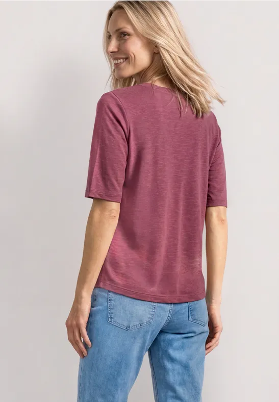 Femme de dos portant un t-shirt rose à manches courtes et un jean bleu clair.