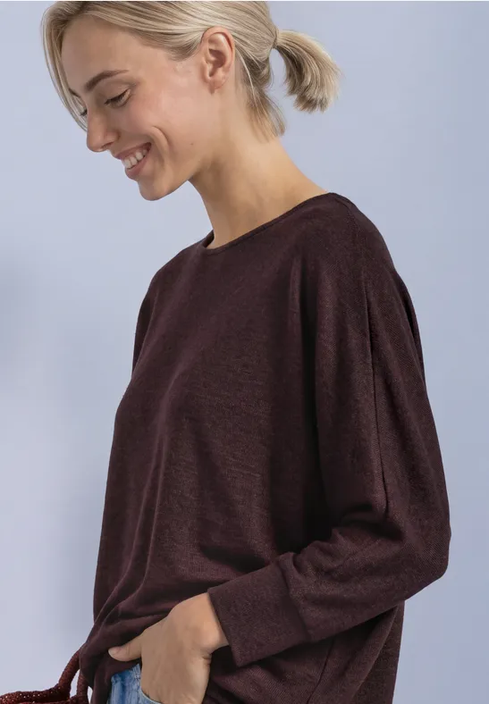 Frau mit hellem Pferdeschwanz trägt ein langärmeliges, burgunderfarbenes Shirt und lächelt im Profil.
