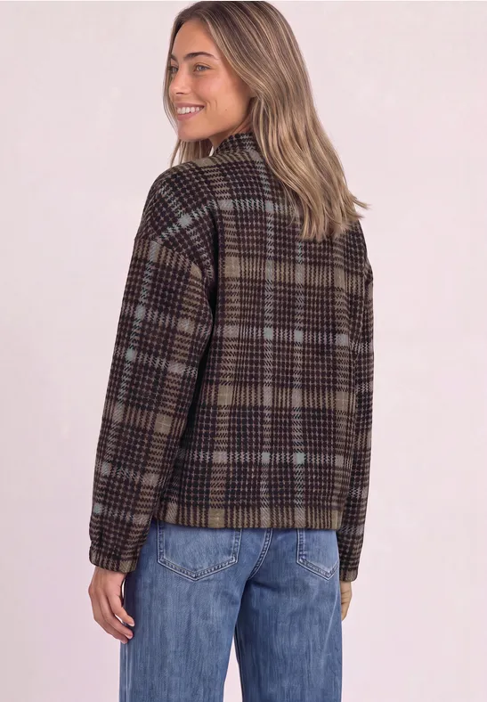 Frau mit kariertem Blouson und Jeans, steht seitlich, lächelt.