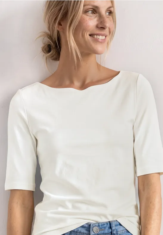 Personne portant un t-shirt blanc à manches trois-quarts devant un fond clair.