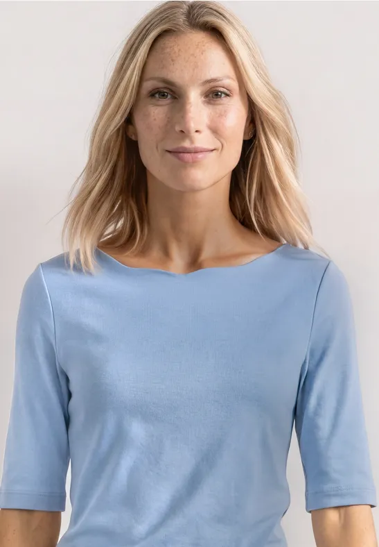 Vrouw in lichtblauw driekwartsmouwshirt tegen effen achtergrond