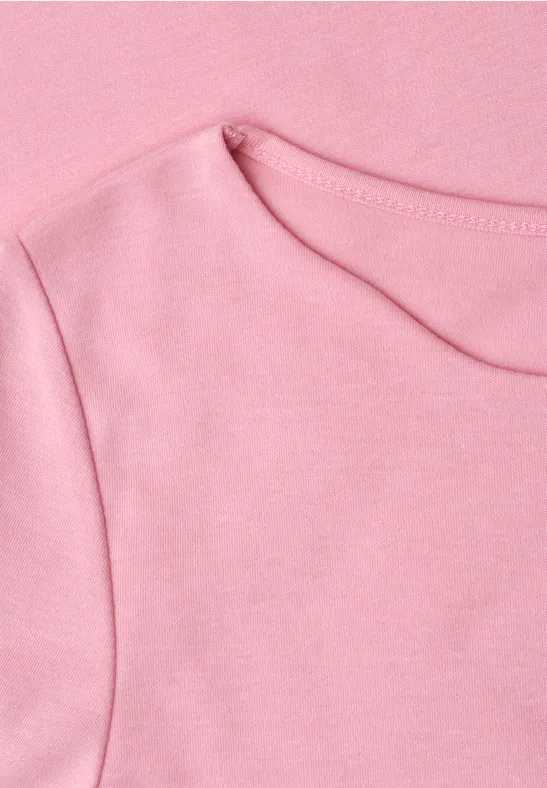 Gros plan d’un T-shirt rose avec encolure ronde et coutures apparentes.