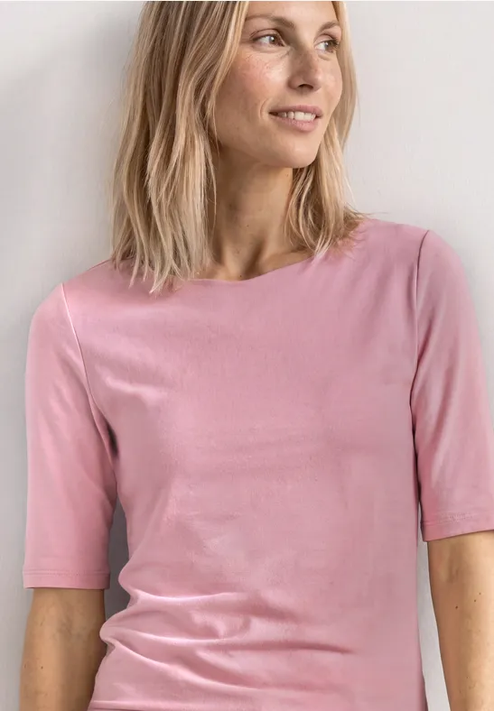 Personne porte un t-shirt rose cintré et cheveux mi-longs devant un fond clair.