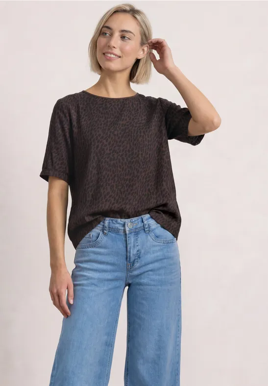Femme en t-shirt noir à motif et jean bleu devant un fond clair.