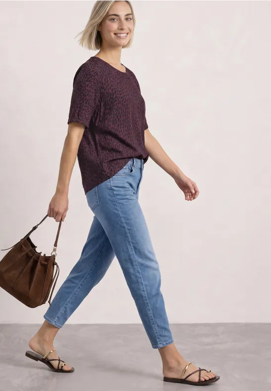 Femme en chemise violette, jean bleu et sandales, portant un sac marron en marchant