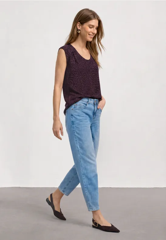 Femme en haut sans manches violet, jean bleu et chaussures slingback noires sur fond blanc.