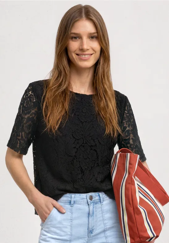 Frau in schwarzer Spitzenbluse und Jeans trägt eine rot-weiß gestreifte Tasche.