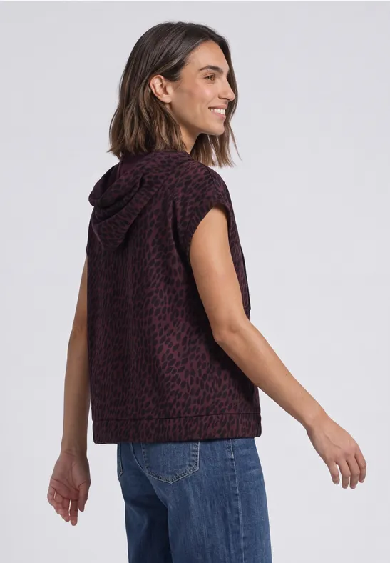 Eine Frau trägt ein ärmelloses Kapuzen-Top mit Leopardenmuster und Jeans.