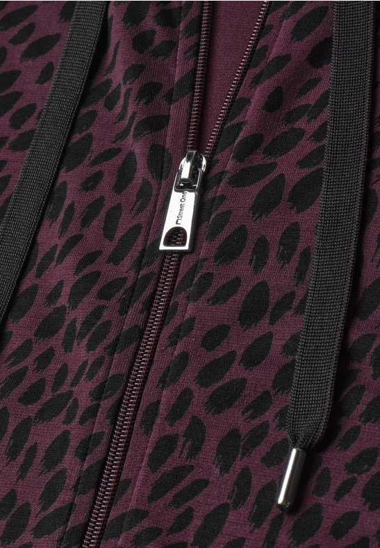 Nahaufnahme eines violetten Stoffes mit schwarzem Leopardenmuster, Reißverschluss und Kordeln.