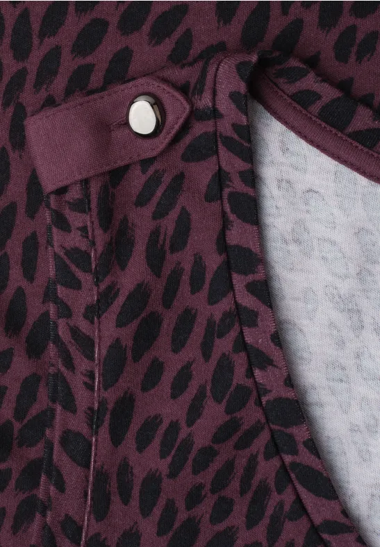 Close-up van een paars shirt met zwart stippenpatroon en decoratieve knoop bij de hals
