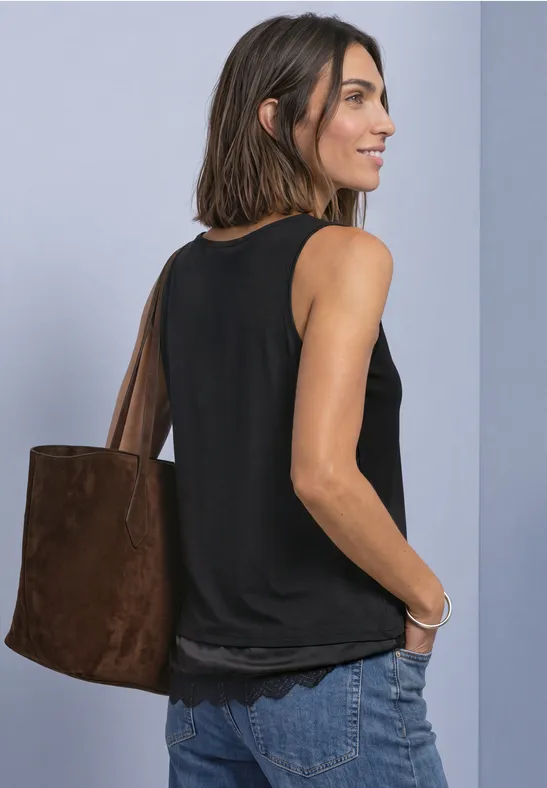 Frau in schwarzem Top und Jeans, mit brauner Tasche über der Schulter, blickt seitlich lächelnd.