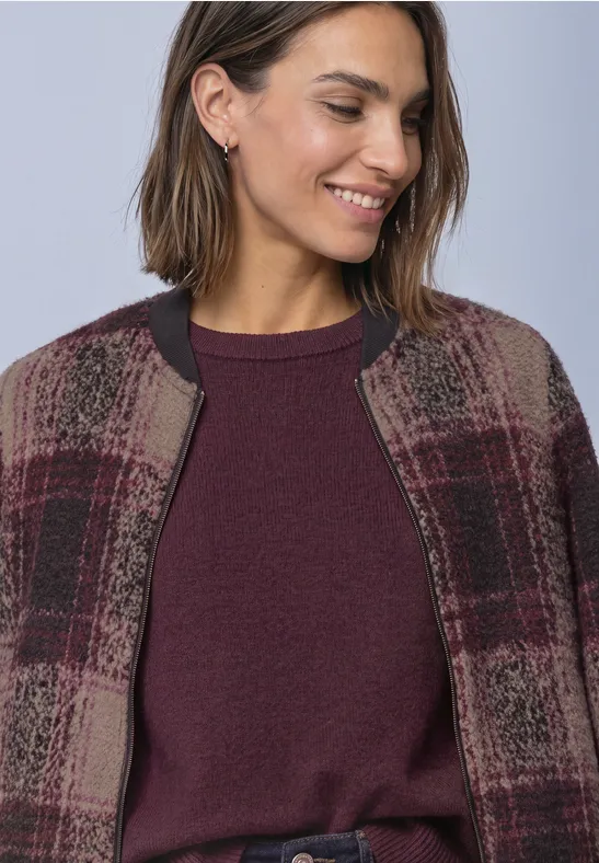 Femme souriante portant un pull bordeaux et une veste à carreaux.