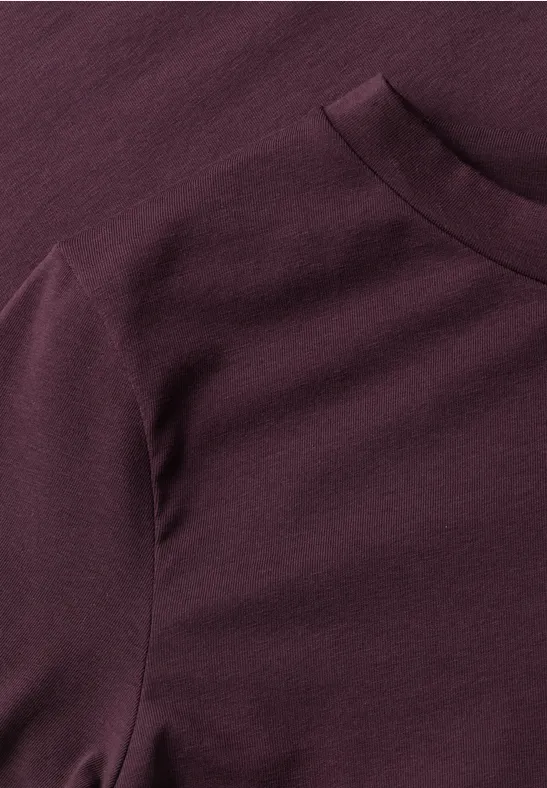 Nahaufnahme eines burgunderfarbenen T-Shirts aus Baumwollstoff mit Rundhalsausschnitt.